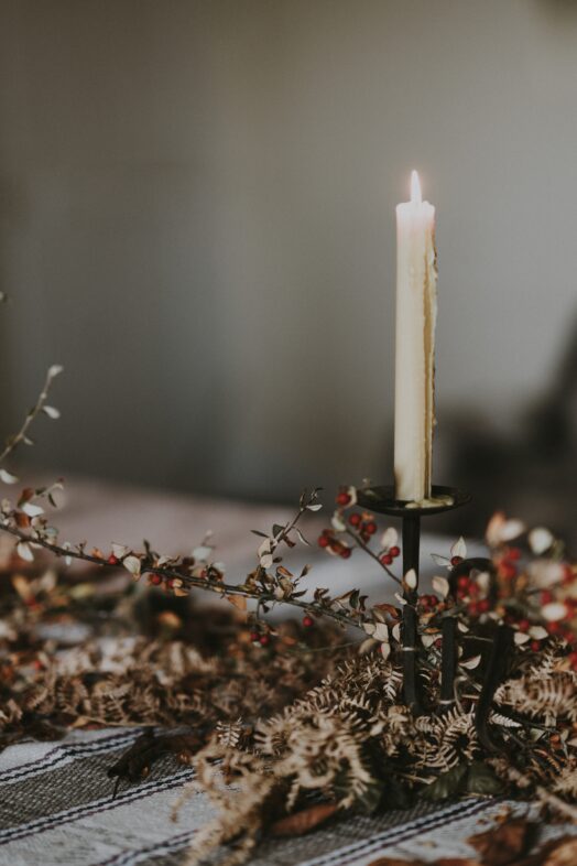 Ett ensamt brinnande ljus står i en ljusstake omgivet av torkade blommor på ett bord.