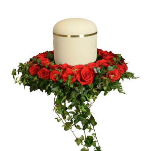 En rund urna med gulddetaljer står på en krans av röda rosor och gröna murgrönor.